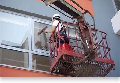 photo of a man in a bucket lift cleaning large windows on a tall building 