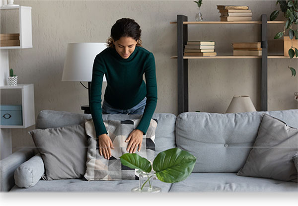 cleaning woman fluffing up livingroom couch pillows 